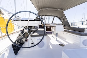 A sailboat's interior with a steering wheel, a cushioned seating area, and a small table. - Sun-kissed Sailing Adventure in Split-Dalmatia, Croatia (Trogir)