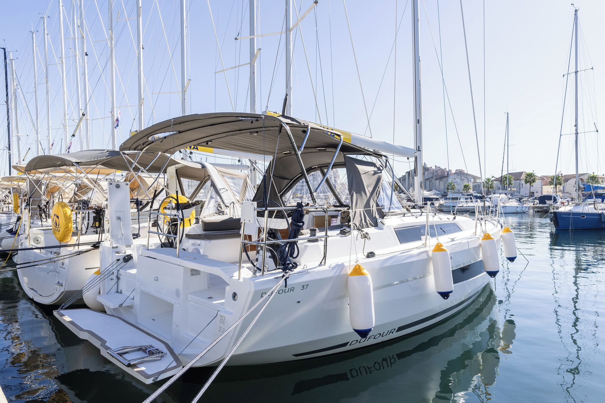 A sailboat docked at a marina with other boats, a clear sky, and calm water.