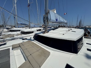 Ein Yachthafen mit mehreren Segelbooten an den Liegeplätzen, einem überdachten Bereich mit Sitzgelegenheiten und blauem Himmel.