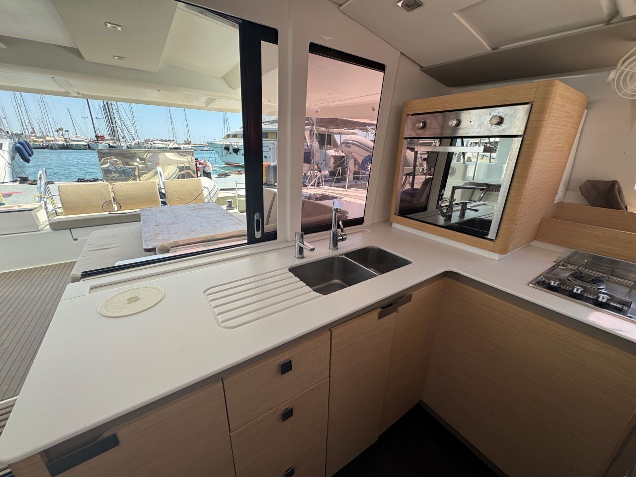 Een kleine kombuis met een spoelbak, fornuis en opbergkasten, met uitzicht op een jachthaven.