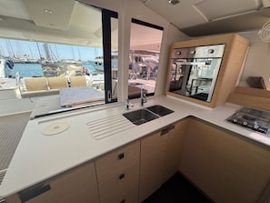 A compact galley with a sink, stove, and storage cabinets, overlooking a marina. - Sun-Kissed Sailing Adventure in Islas Baleares, Mallorca (Palma)