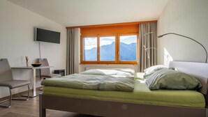 A hotel room with a bed, a desk, a chair, a TV, and a window with a mountain view.