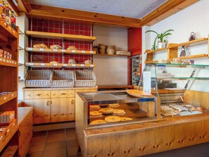 A bakery with wooden shelves displaying bread and pastries, wicker baskets, and a glass display case with cakes.