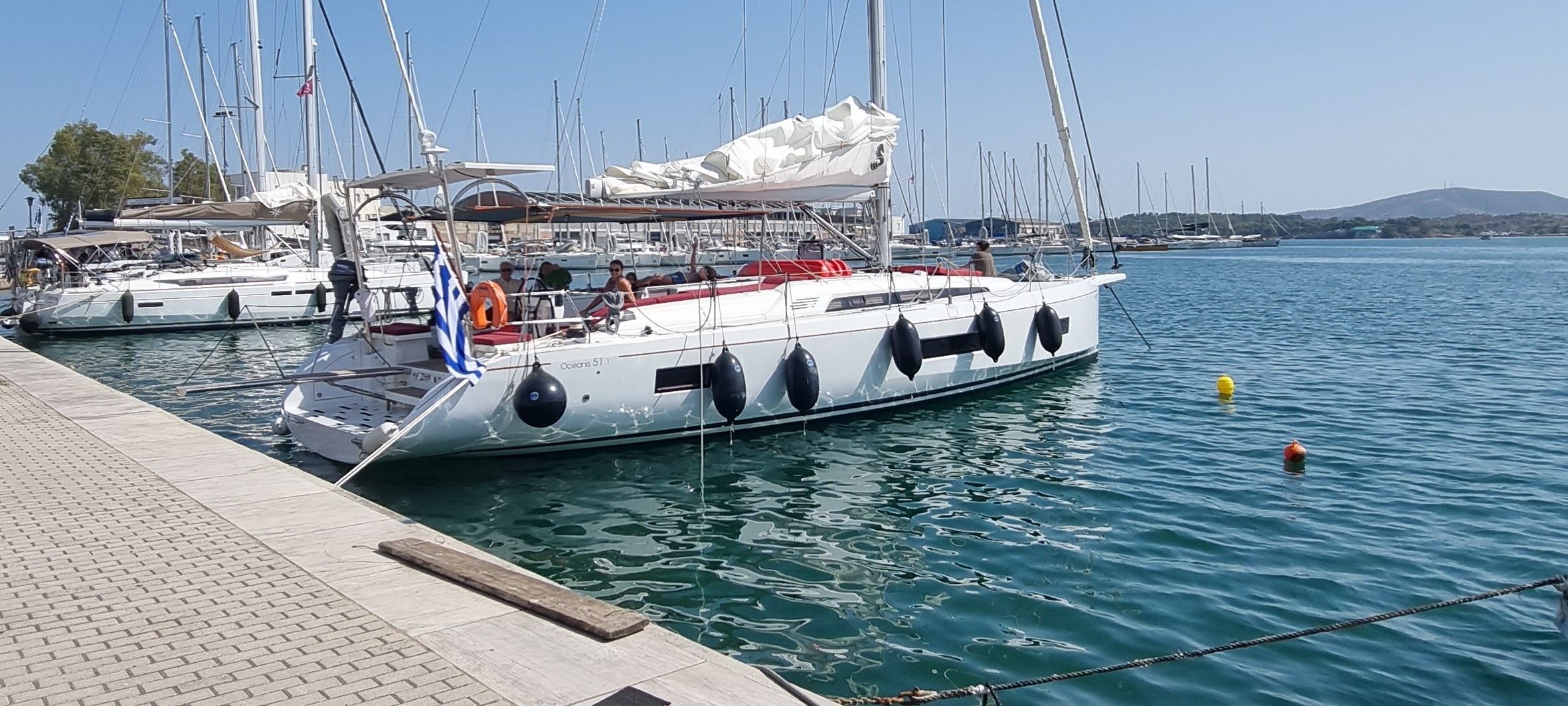 A marina with multiple sailboats docked, a clear sky, and calm water.