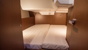 A compact bed with a textured mattress, a headboard, and a door with a handle. - Sun-Kissed Sailing Adventure in the Saronic Islands (Nea Peramos)