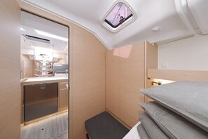 Ein kleines Zimmer mit Bett, einer kleinen Sitzbank, einem Spiegel, einem Fenster und einer Küchenzeile.