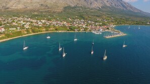 Vue aérienne d’une ville côtière avec un port de plaisance, des bateaux et une chaîne de montagnes en arrière-plan.