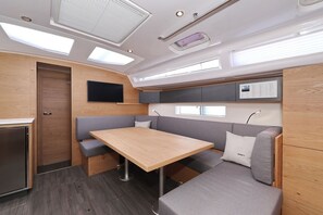 A compact RV interior with a wooden table, gray seating, a TV mounted on the wall, and a window. - Sun-Kissed Sailing Adventure in Zadar, Croatia (Biograd na moru)