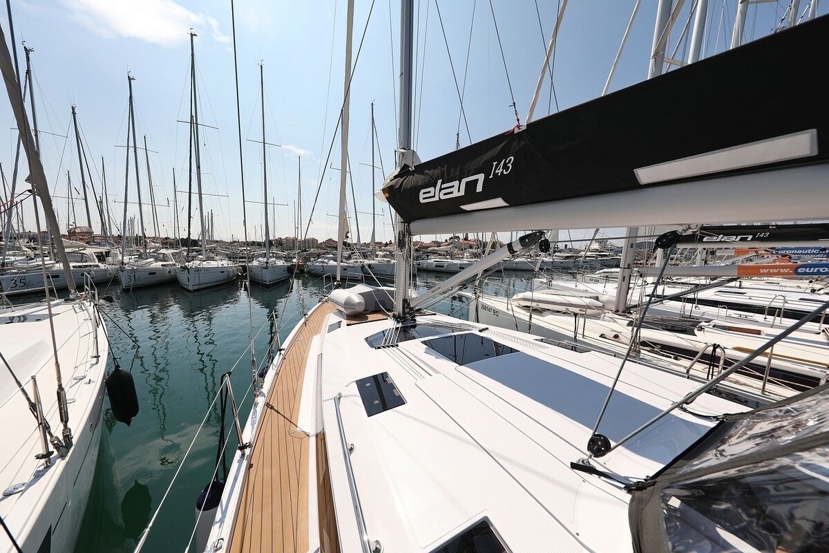 Un port de plaisance où sont amarrés de nombreux voiliers, une terrasse en bois et un ciel dégagé.