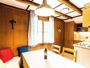 Ein gemütliches Zimmer mit Holzwänden, einem Esstisch mit Stühlen, einem Fenster mit Vorhängen und einer Küchenzeile mit Herd.