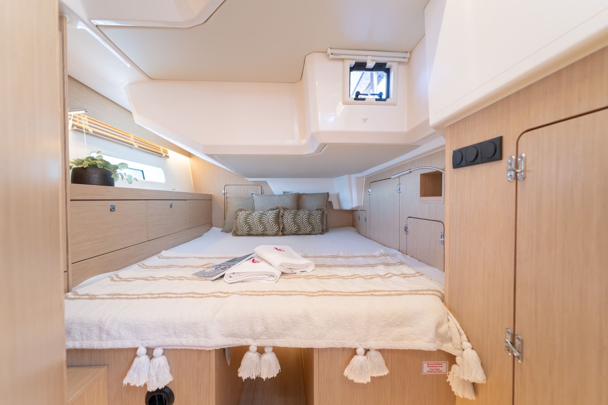 Un interior compacto y bien iluminado con una cama, armarios de almacenamiento y una ventana pequeña.