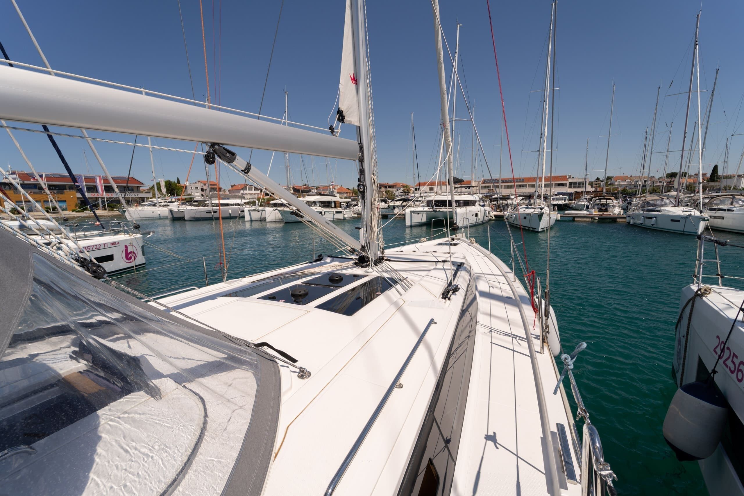 A marina with multiple sailboats docked, clear skies, and buildings in the background.