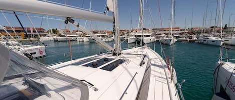 A marina with multiple sailboats docked, clear skies, and buildings in the background.
