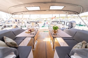 Ein Bootsdeck mit zwei Tischen, gepolsterten Sitzgelegenheiten und Blick auf andere Boote.