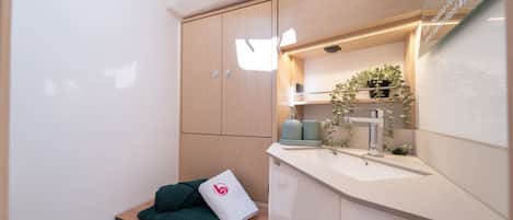 A compact bathroom with a wooden cabinet, a shelf with towels, a sink, and a mirror.