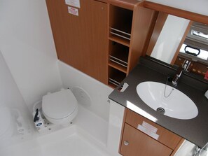 Ein kleines Badezimmer mit Toilette in Weiß, einem Waschbecken mit schwarzer Arbeitsplatte und Holzschränken.