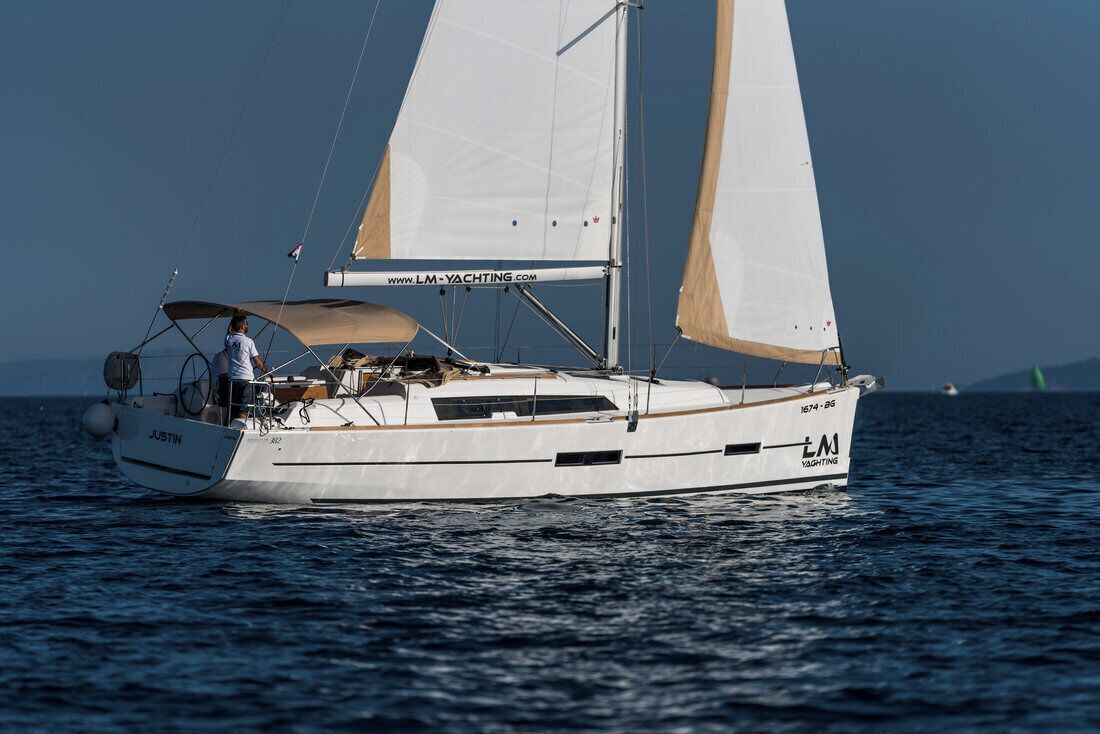 Un voilier avec une cabine, une personne sur le pont et une adresse de site web inscrite sur la voile.