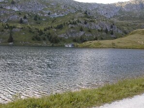 Un lago con una casa pequeña en la orilla, rodeado de montañas y vegetación.