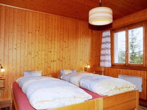 Un dormitori de cabana de fusta amb dos llits, una finestra amb cortines i una làmpada penjant.