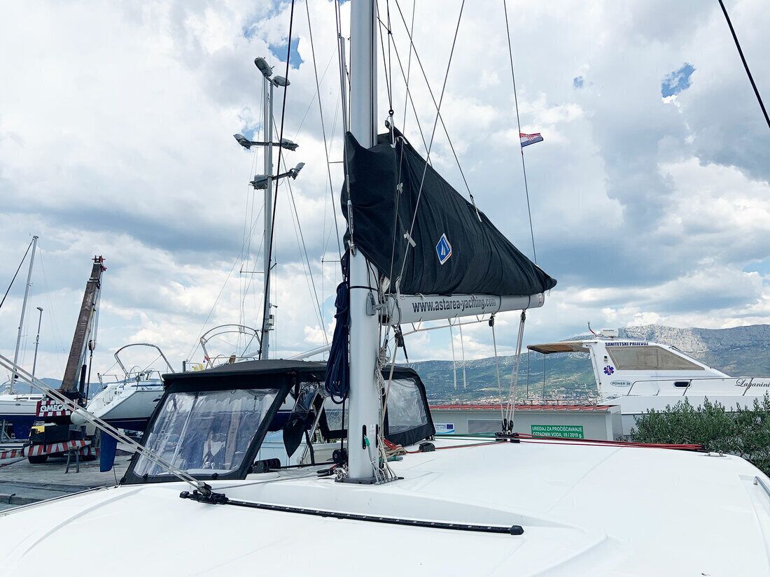 Ein Segelboot liegt an einem Steg, mit einer Internetadresse, einem Mast und einer bergigen Landschaft im Hintergrund.