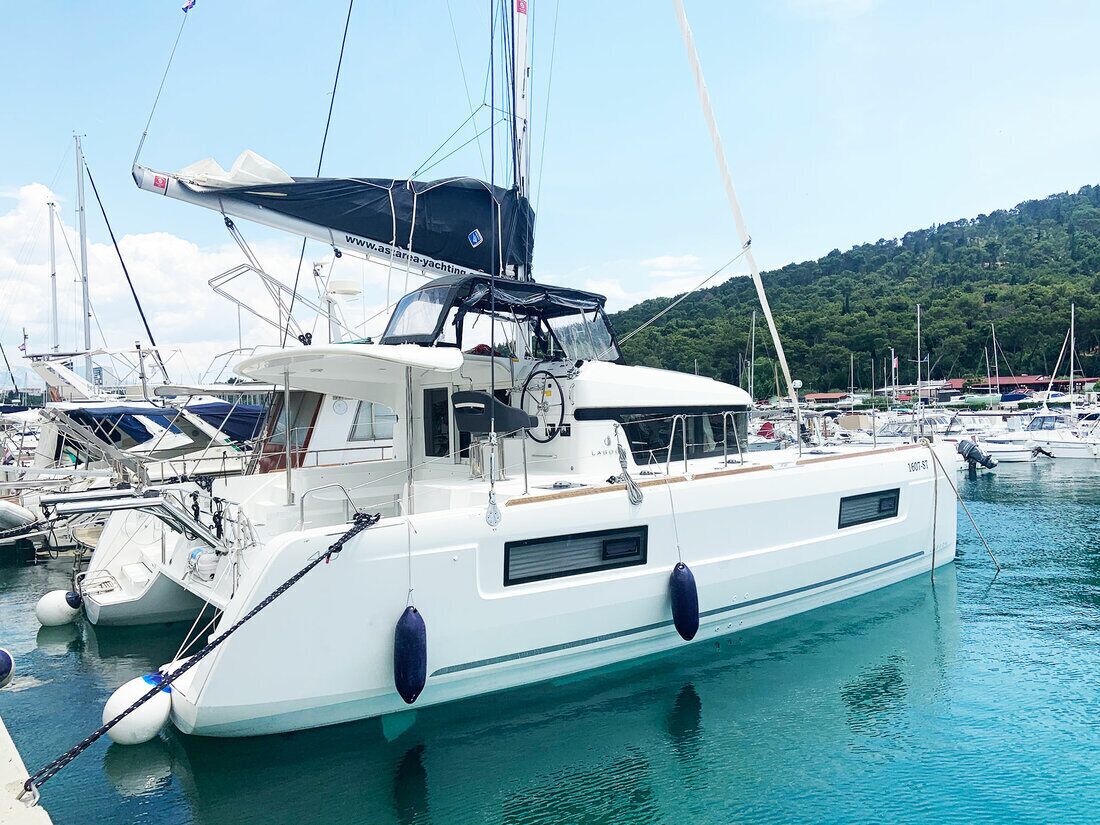 Un port de plaisance où un yacht blanc est amarré, entouré d’autres bateaux, avec une colline boisée en arrière-plan.