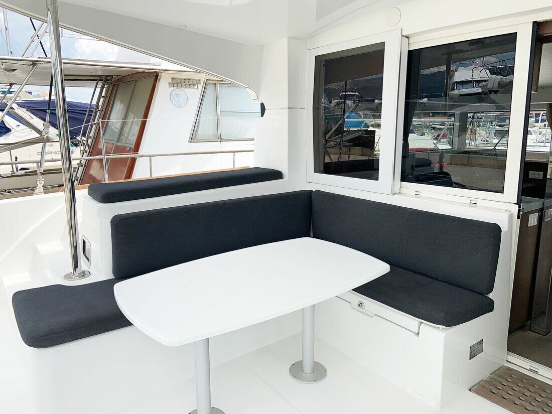 Bootinterieur met een witte tafel, donkere gestoffeerde zitplaatsen en een raam met uitzicht op andere boten.
