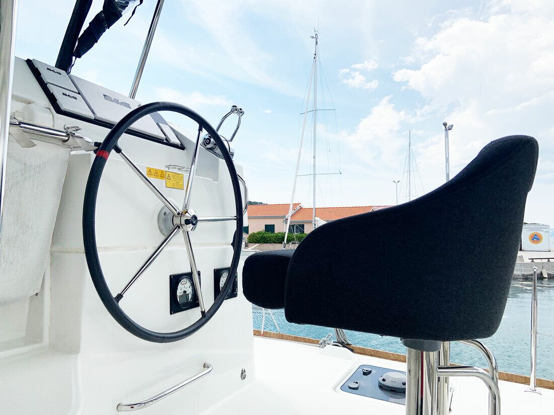 Steuerstand eines Bootes mit Steuer, gepolstertem Sitz und Blick auf den Hafen mit anderen Booten und Gebäuden.