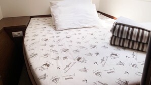 Ein Einzelbett mit weißem Kopfkissen und einer gestreiften Decke, ein Nachttisch und eine wandmontierte Lampe.
