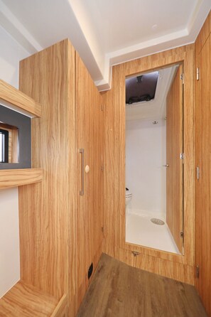 Un baño pequeño con tocador de madera, cabina de ducha y una ventana.
