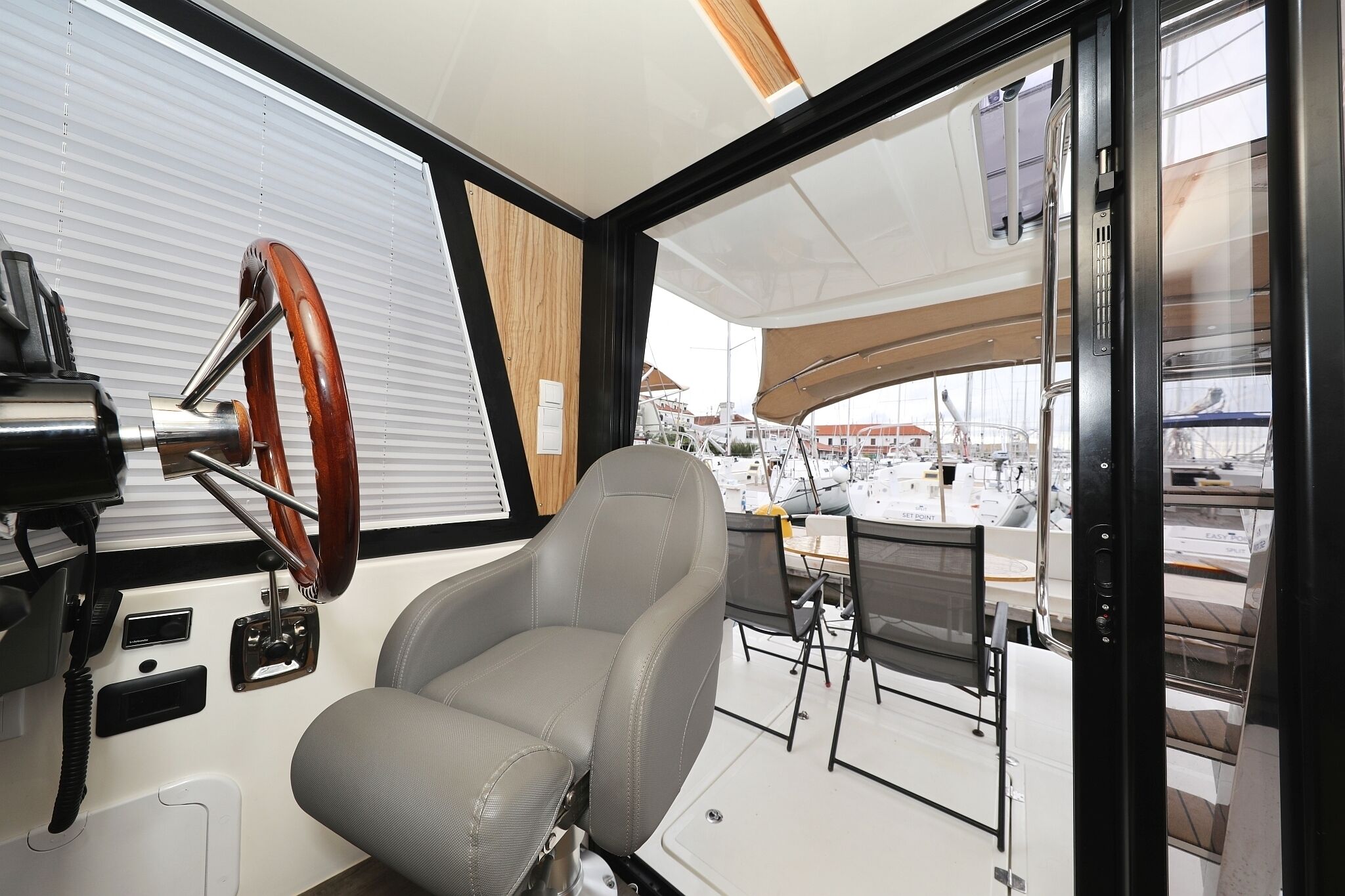 Interior de barco com timão, painel de controle e área de refeições com mesa e cadeiras.