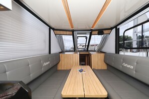 Ein modernes Interieur mit einem zentralen Tisch, grau gepolsterten Sitzgelegenheiten und großen Fenstern, die einen Blick nach außen bieten.
