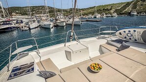 A marina with multiple sailboats docked, a boat's deck with seating and a bowl of fruit, and a hilly landscape in the background. - Sun-Kissed Sailing Adventure in Sibenik, Croatia (Primošten)