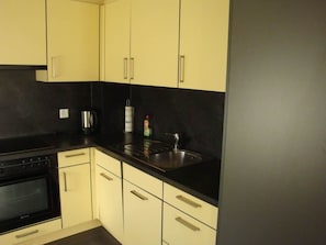 Een keuken met een zwart aanrecht, een roestvrijstalen spoelbak, een waterkoker en een fles afwasmiddel.