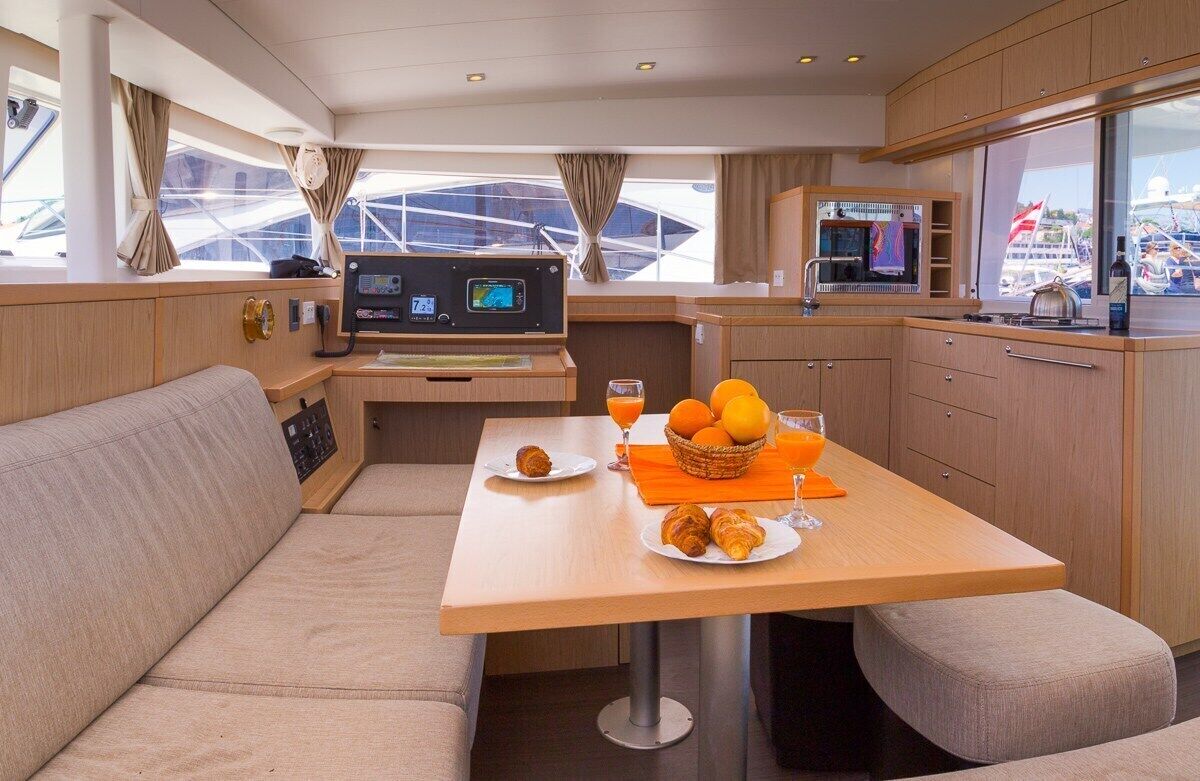 A yacht interior with a dining area, a control panel, and a view of the marina.