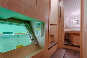 Un interior compacte i ben il·luminat amb una llitera, una taula petita i una finestra amb persianes.