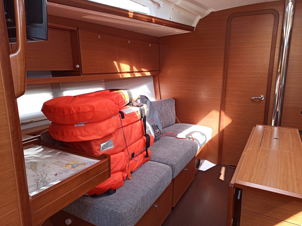 A compact RV interior with a sofa, a table, and a storage area with a red bag.