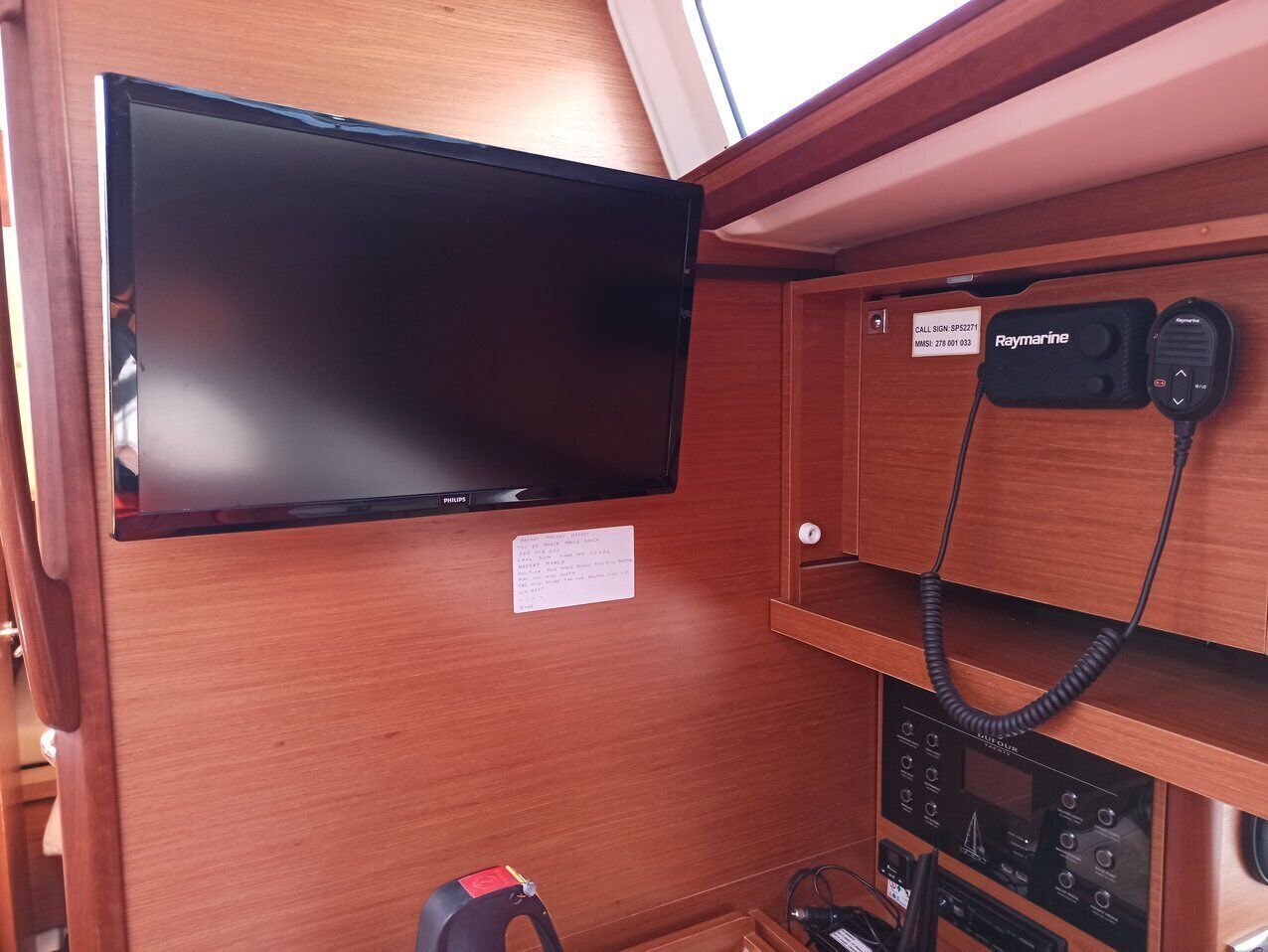 Een houten interieur met een wandtelevisie, een Raymarine-apparaat en een bedieningspaneel.