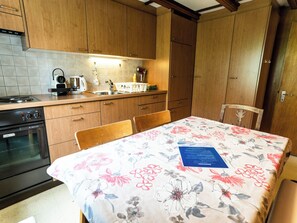 A kitchen with wooden cabinets, a stove, and a table with a floral tablecloth. - Bürcher Haus 1. OG Süd-West Appartement/Fewo, Dusche, WC by Interhome (Riederalp)