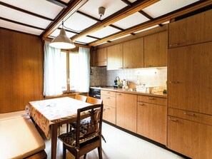 A kitchen with wooden cabinets, a dining table with a floral tablecloth, and a chair with a cushion. - Bürcher Haus 1. OG Süd-West Appartement/Fewo, Dusche, WC by Interhome (Riederalp)