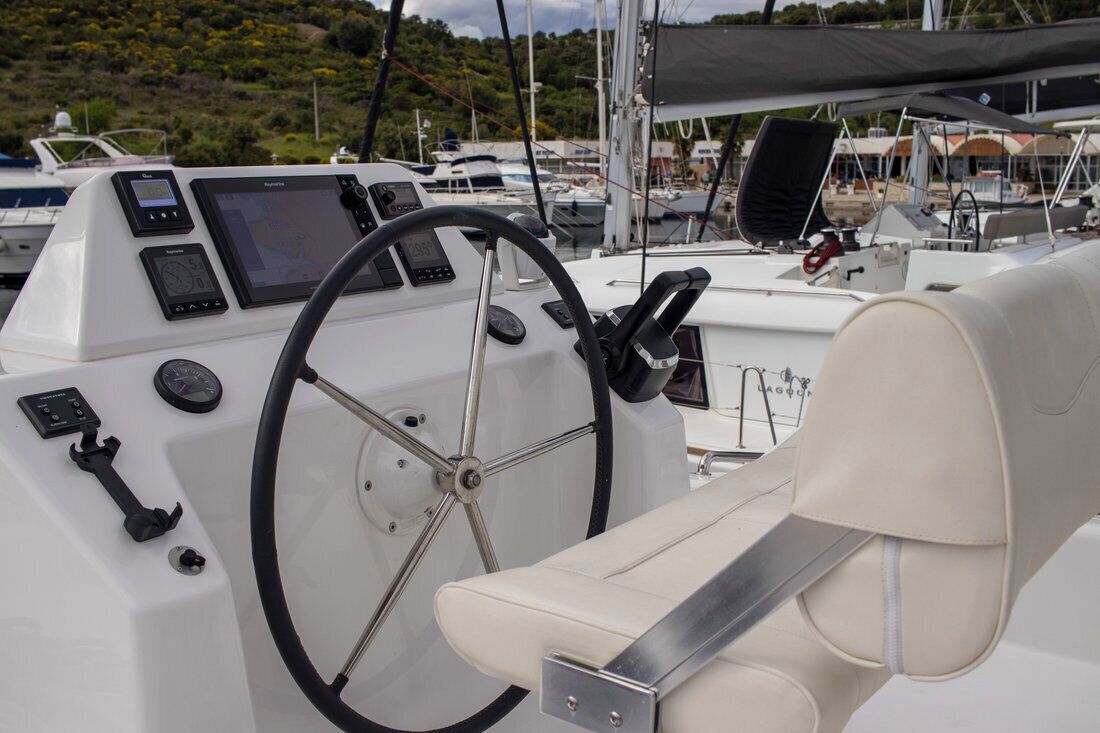 Posto de comando de um barco, com leme, telas de navegação e assento acolchoado.