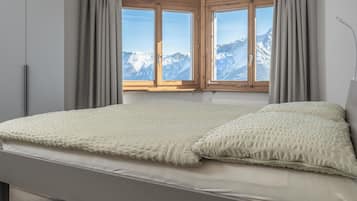 A bedroom with a bed, a view of snow-capped mountains, and a window with wooden shutters.