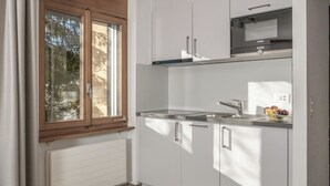 A modern kitchen with white cabinets, a stainless steel sink, and a window with a view of trees.