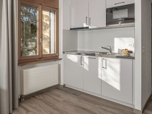 A modern kitchen with white cabinets, a stainless steel sink, and a window with a view of trees.