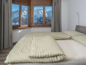 A bedroom with a bed, curtains, and a view of snow-capped mountains through large windows. - Zurschmitten 12 1. UG Süd Appartement/Fewo, Dusche, WC by Interhome (Riederalp)