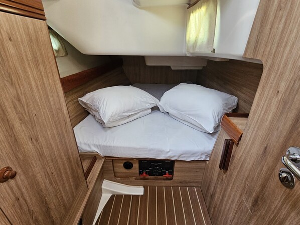 A compact, wooden interior of a boat cabin with a bed, pillows, a control panel, and a small window. - Sun-Kissed Sailing Adventure in Zadar, Croatia (Biograd na moru)