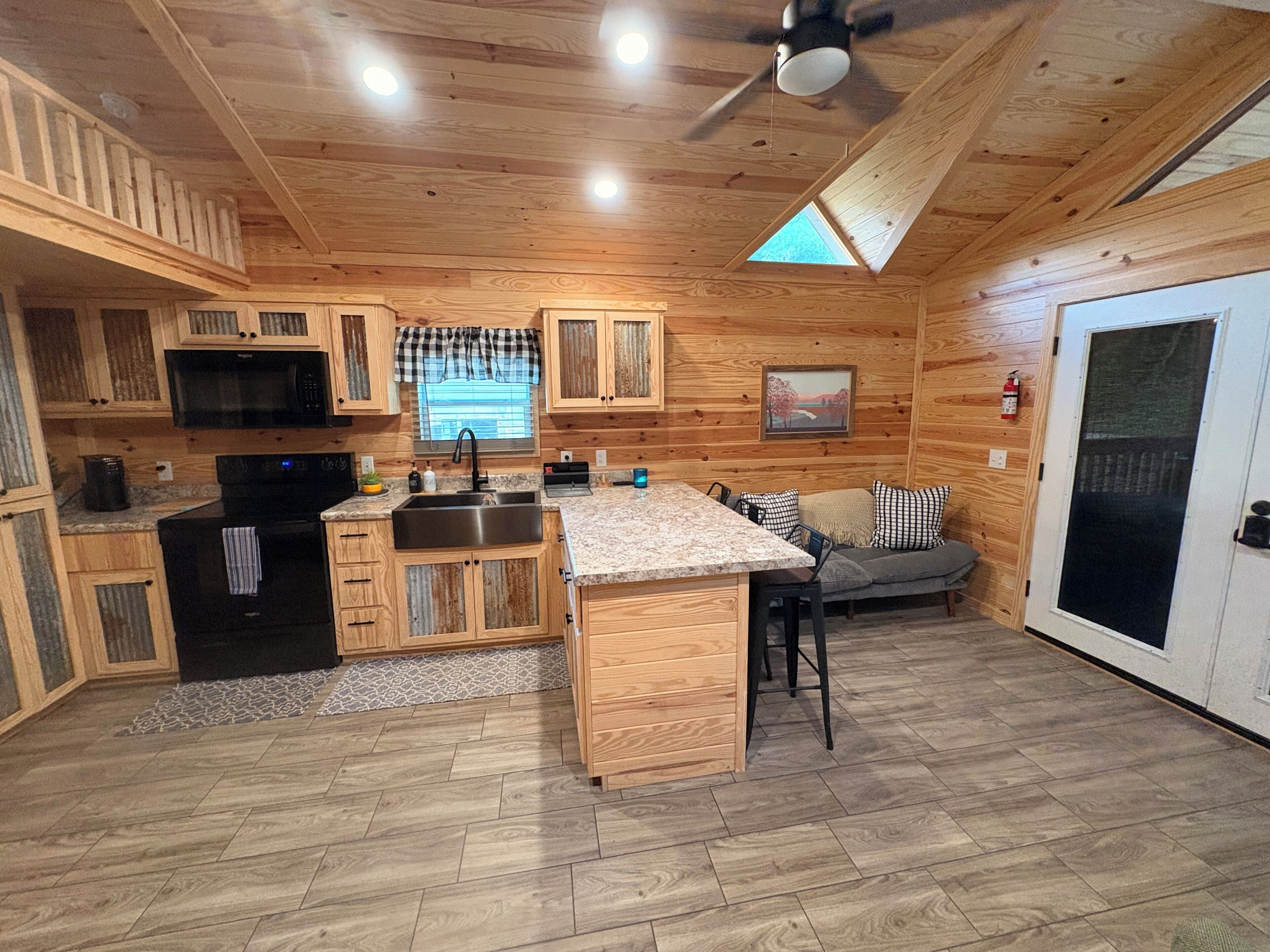 Interior de una cabaña de madera con cocina, comedor y un gran ventanal corredero.