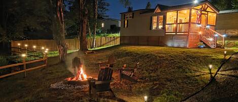 A house with a deck, a fire pit, and a well-lit backyard.