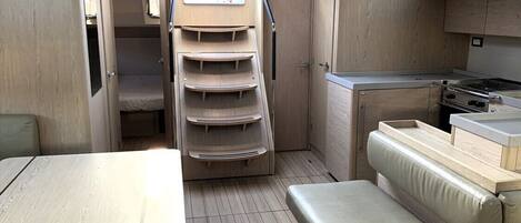 Un interior compacto con una mesa de comedor, un banco acolchado, una zona de cocina con estufa y un ventanal pequeño.