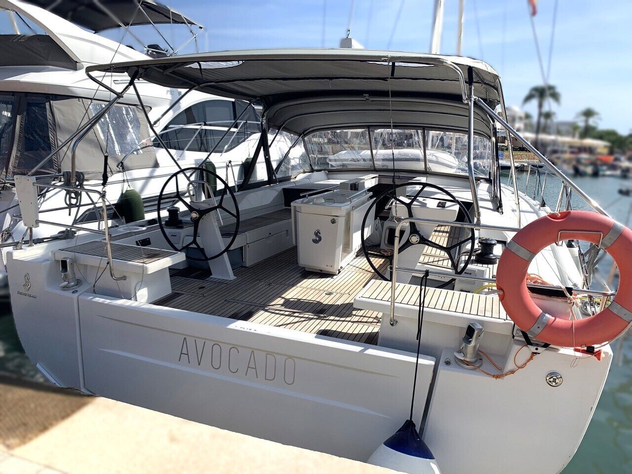 Eine Yacht namens 'AVOCADO' liegt in einer Marina festgemacht, mit überdachter Deckfläche, Rettungsboje und diverser nautischer Ausrüstung.