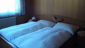 A bedroom with a wooden headboard, a bed with white bedding, a bedside lamp, and a window with curtains. - Abendrot 1. OG Süd-West Appartement/Fewo, Dusche oder Bad, WC by Interhome (Riederalp)